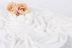 two pink roses resting on a white, crumpled fabric.