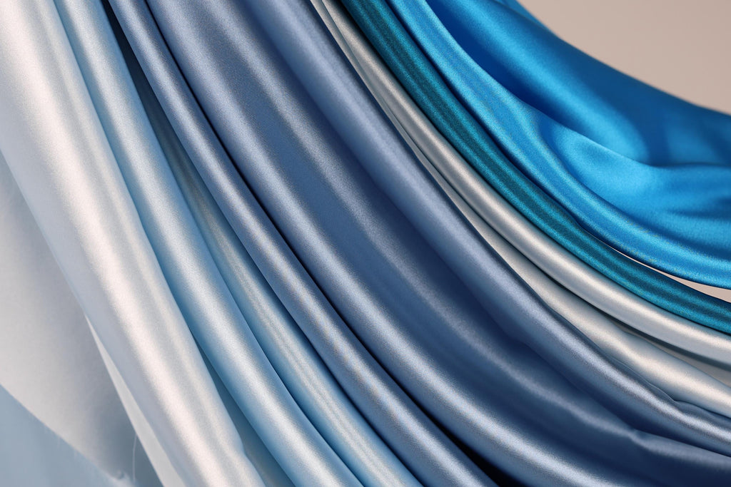 a close-up view of a collection of blue and silver satin fabric, with the fabric appearing to be folded or draped in a cascading manner.