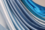 a close-up view of a collection of blue and silver satin fabric, with the fabric appearing to be folded or draped in a cascading manner.
