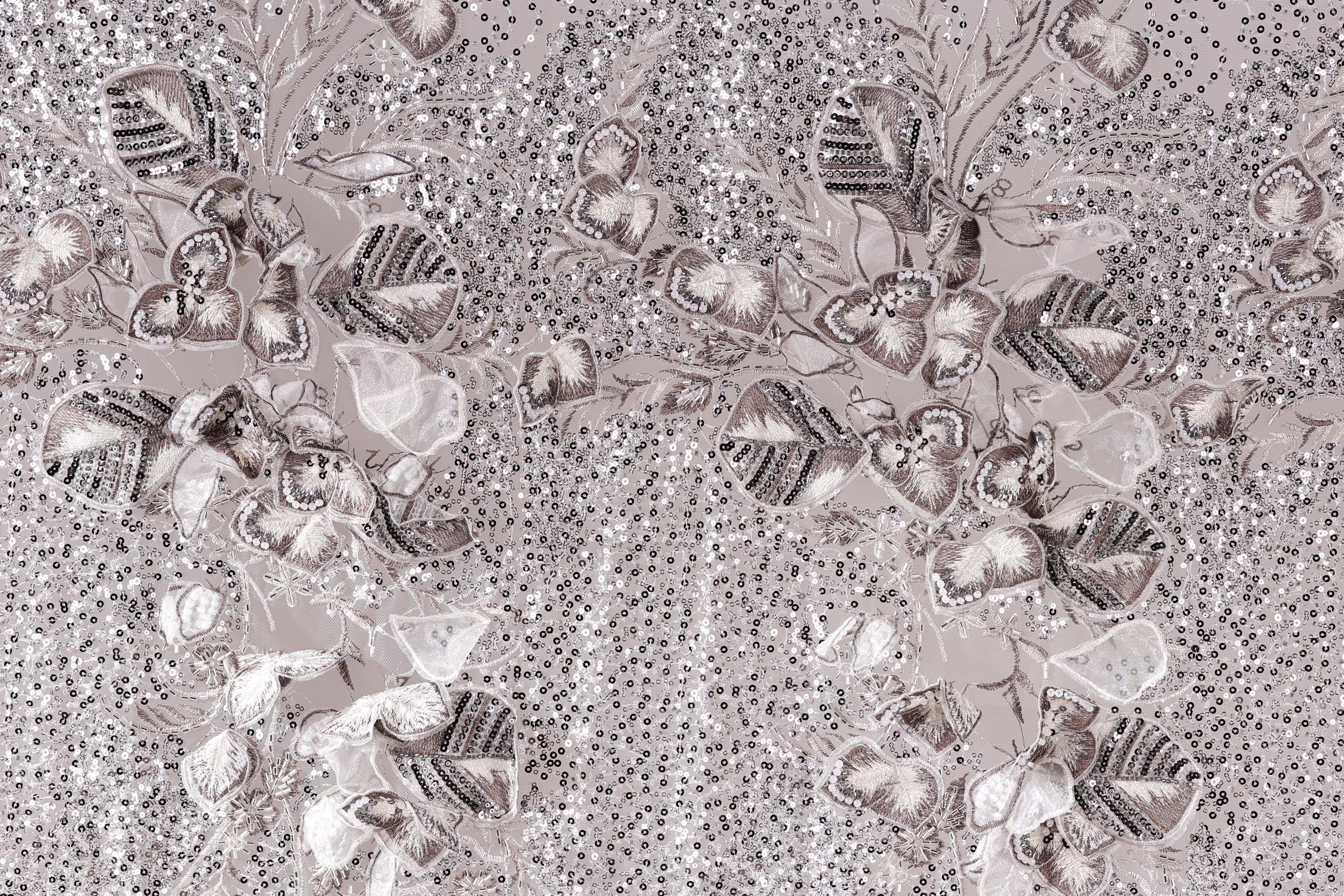 The image is a close-up of a fabric with a floral pattern, featuring a variety of leaves and flowers in shades of gray and white. The pattern is intricate and detailed, with the leaves and flowers arranged in a visually appealing manner. The background of the image is a light gray color, which contrasts with the darker tones of the floral pattern. The overall composition of the image is balanced and harmonious, with the floral pattern taking center stage.