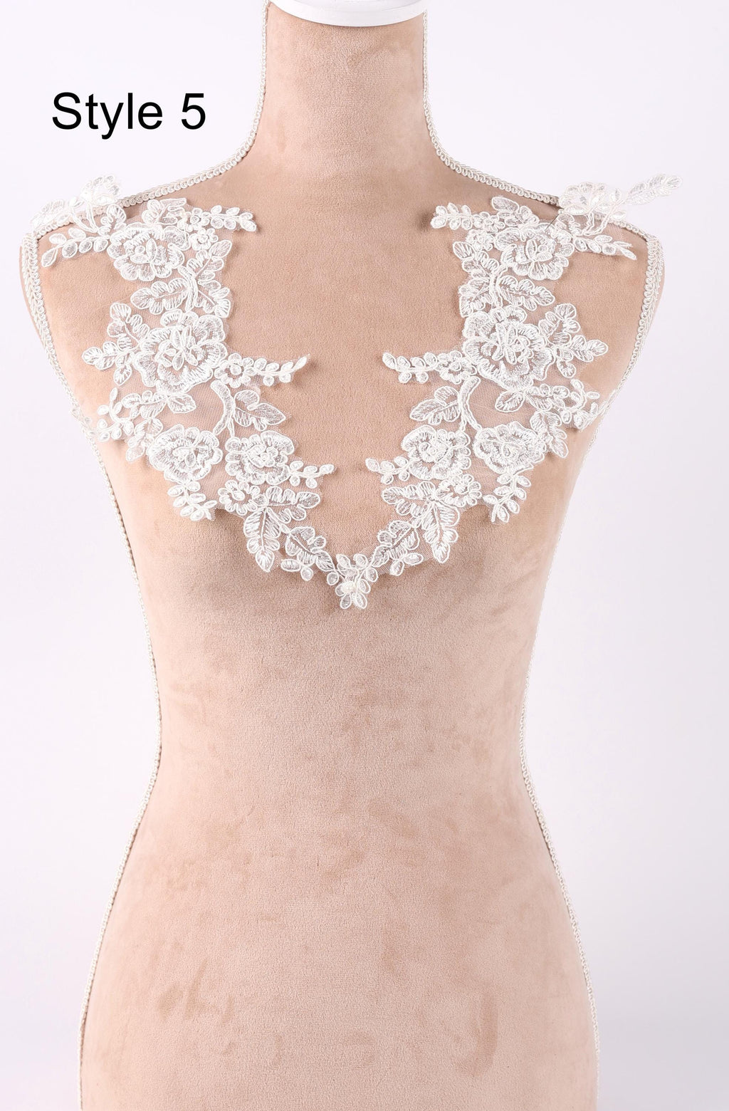 A mannequin wearing a beige dress with a white lace collar and floral embellishments.