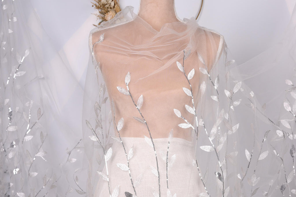 A mannequin wearing a white dress with a sheer, leaf-like veil draped over it.
