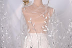 A mannequin wearing a white dress with a sheer, leaf-like veil draped over it.