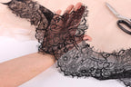A hand holding a piece of black lace with intricate floral patterns, and a pair of scissors is visible in the background.