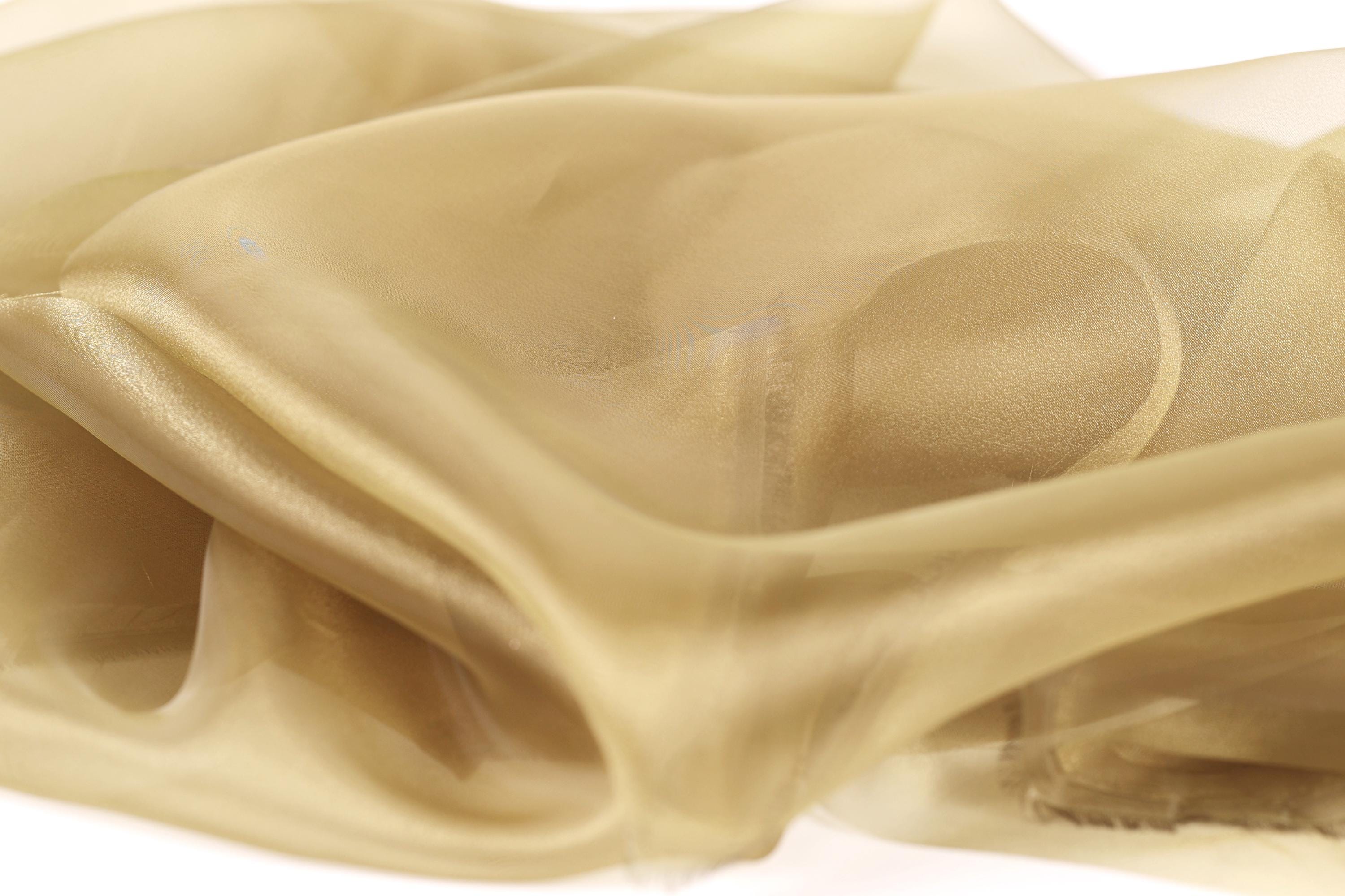The image is a close-up of a light brown fabric, possibly silk or chiffon, with a soft, flowing texture.