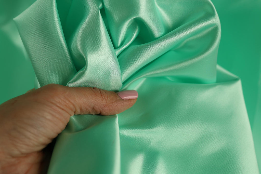 A hand is holding a piece of green satin fabric, with the fingers curled around it.