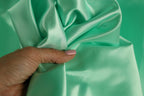 A hand is holding a piece of green satin fabric, with the fingers curled around it.