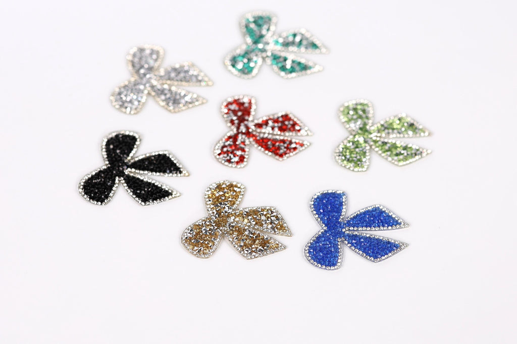 seven glittery, colorful bow-shaped objects arranged on a white background.