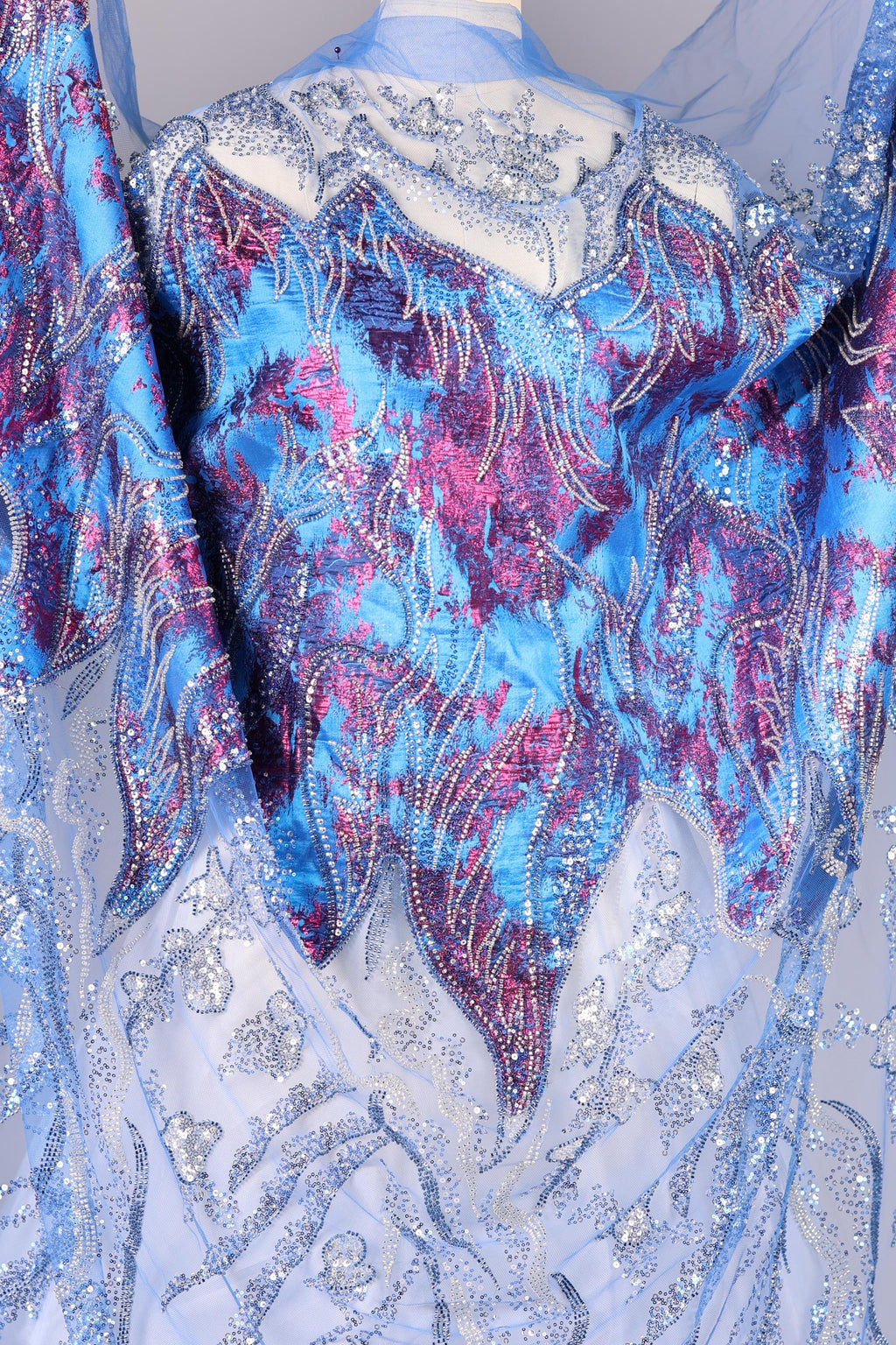 a close-up view of a fabric with a vibrant, multicolored pattern. The fabric appears to be a blend of blue, purple, and pink hues, with intricate designs and embellishments. The fabric is spread out, revealing its detailed and eye-catching appearance.