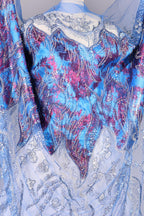 a close-up view of a fabric with a vibrant, multicolored pattern. The fabric appears to be a blend of blue, purple, and pink hues, with intricate designs and embellishments. The fabric is spread out, revealing its detailed and eye-catching appearance.