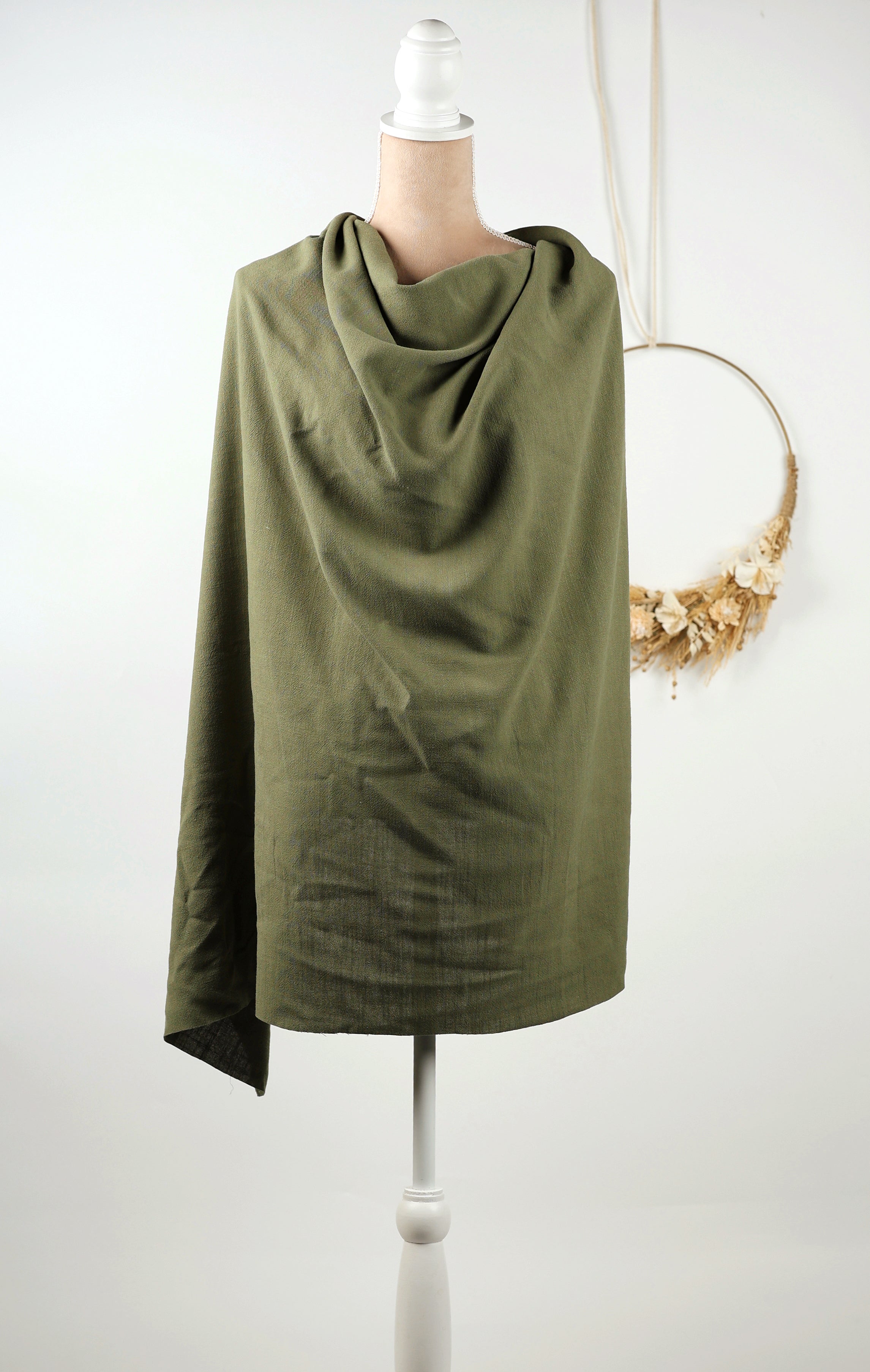 A mannequin wearing a green, loose-fitting garment, possibly a shawl or wrap, is displayed against a white background.