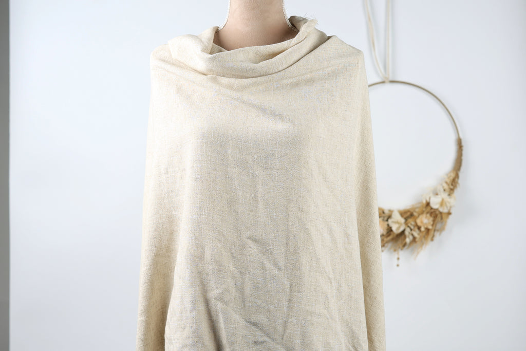 A mannequin wearing a beige shawl stands against a white background, with a wreath hanging on the wall behind it.
