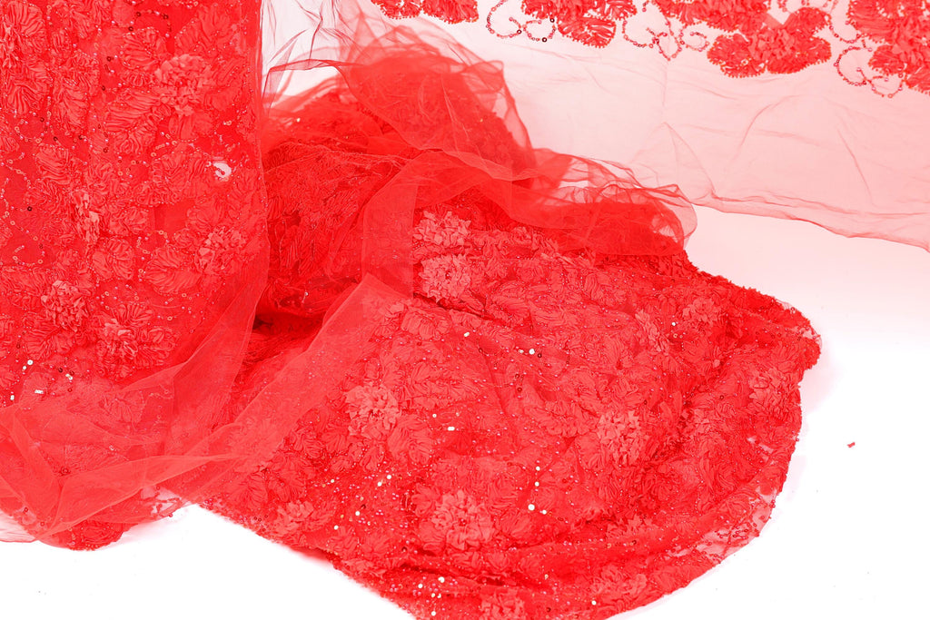The image is a close-up of a red fabric with a floral pattern, featuring a lot of texture and detail.