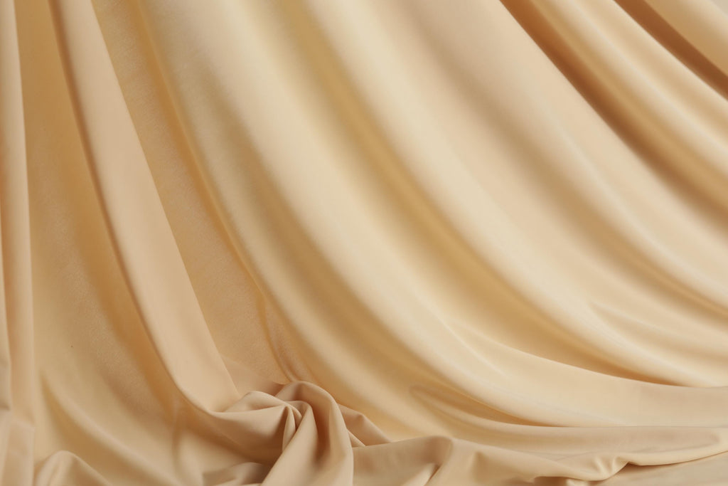 The image is a close-up of a soft, flowing fabric, possibly a sheer or sheer-like material, with a light beige color. The fabric appears to be wrinkled and draped, creating a sense of movement and texture.