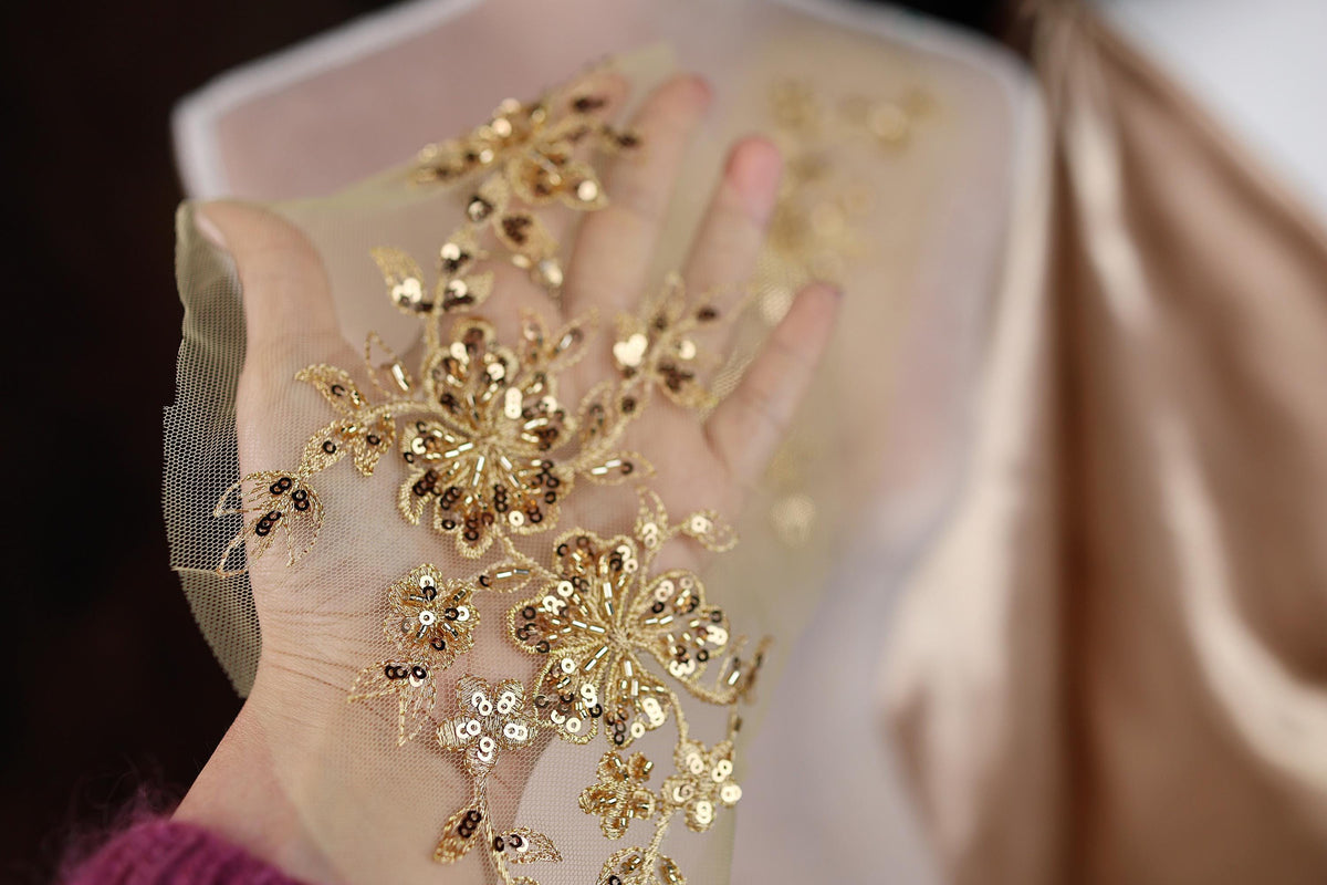 A hand holding a piece of fabric with gold sequin and floral embroidery.