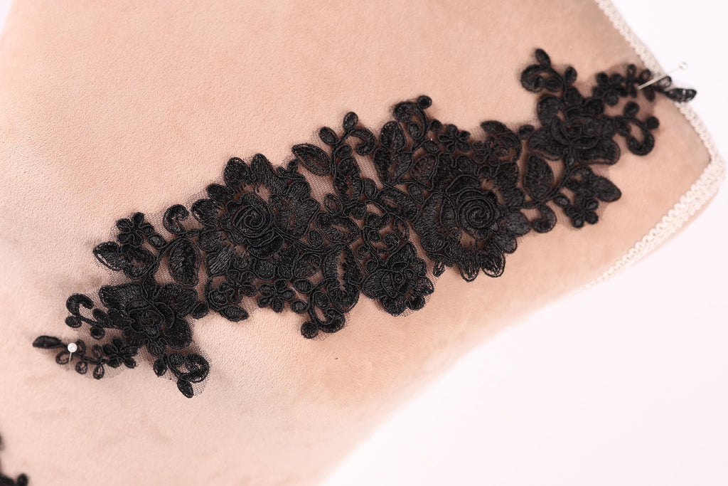 A close-up image of a black lace piece with intricate floral patterns, displayed on a light-colored surface.