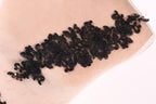 A close-up image of a black lace piece with intricate floral patterns, displayed on a light-colored surface.