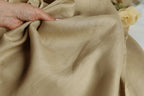 A hand is holding a piece of light brown fabric, which appears to be made of linen.