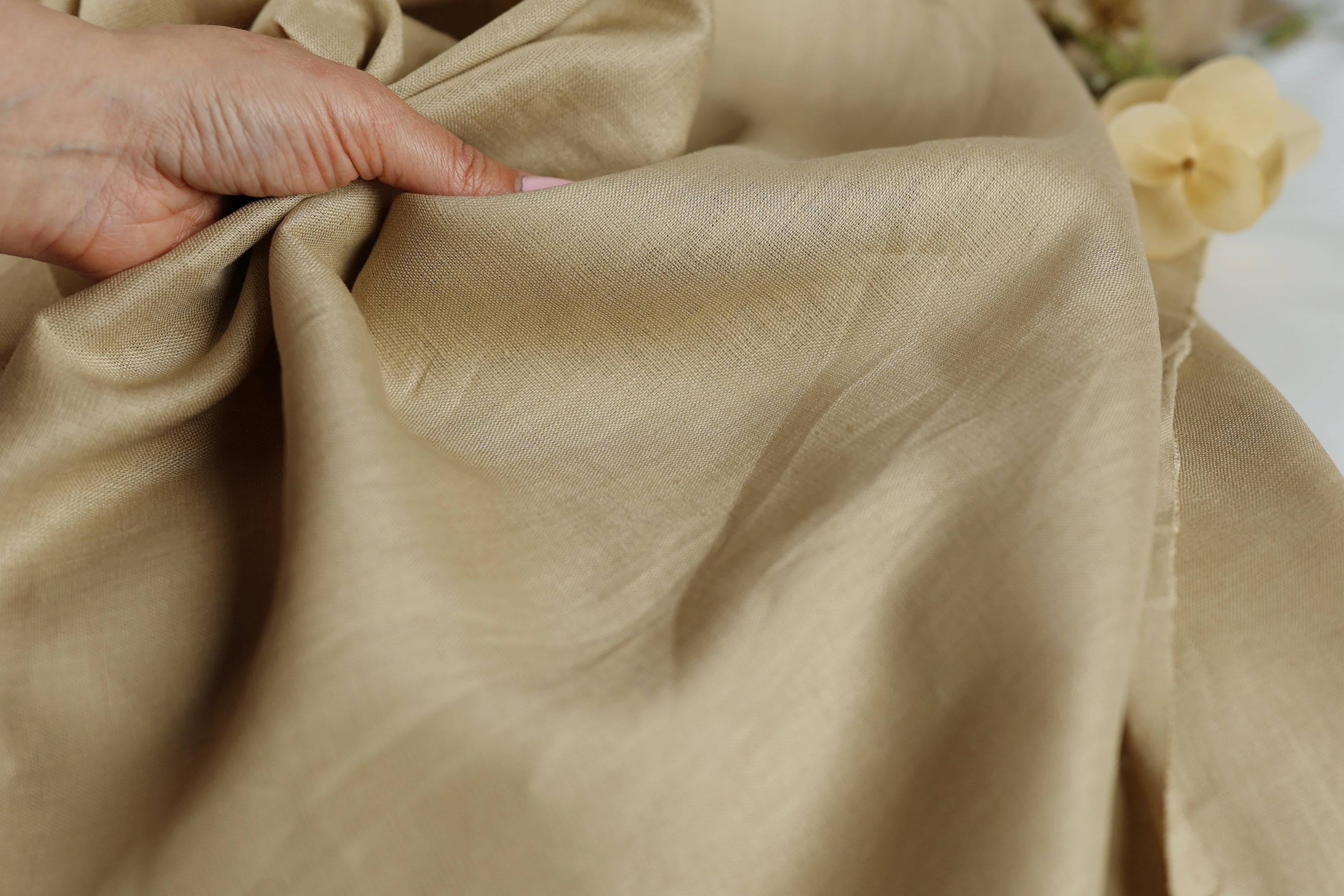 A hand is holding a piece of light brown fabric, which appears to be made of linen.