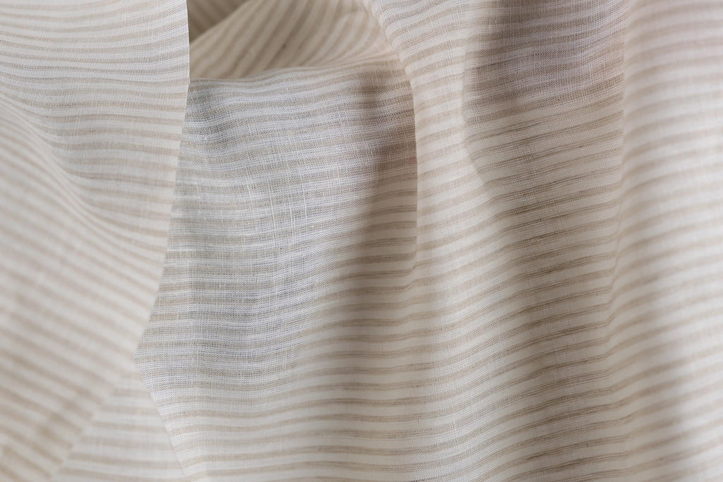a close-up view of a fabric with horizontal stripes in various shades of beige and white. The fabric appears to be soft and delicate, with a slightly wrinkled texture.