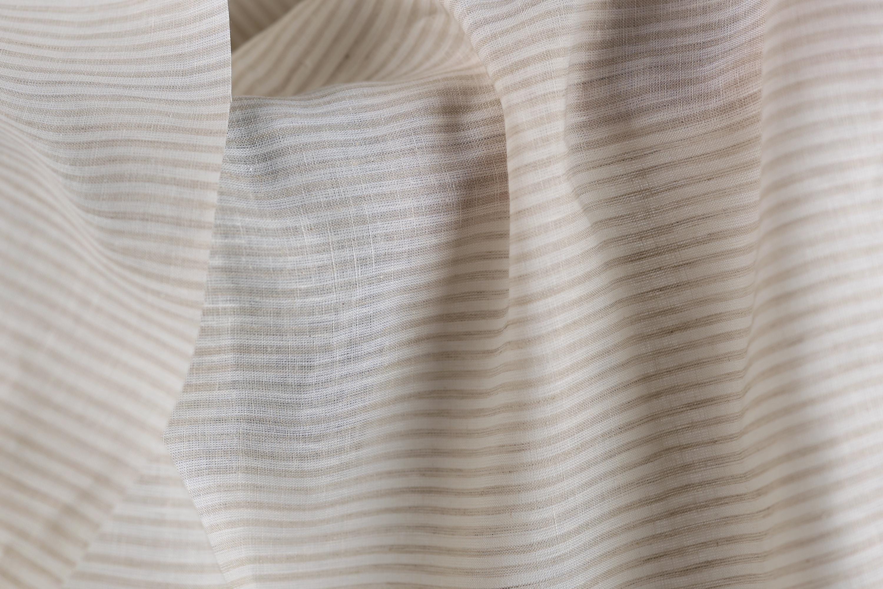 a close-up view of a fabric with horizontal stripes in various shades of beige and white. The fabric appears to be soft and delicate, with a slightly wrinkled texture.