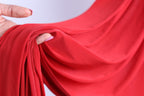A hand is holding a red fabric, with the fingers curled around it, creating a sense of movement and texture.