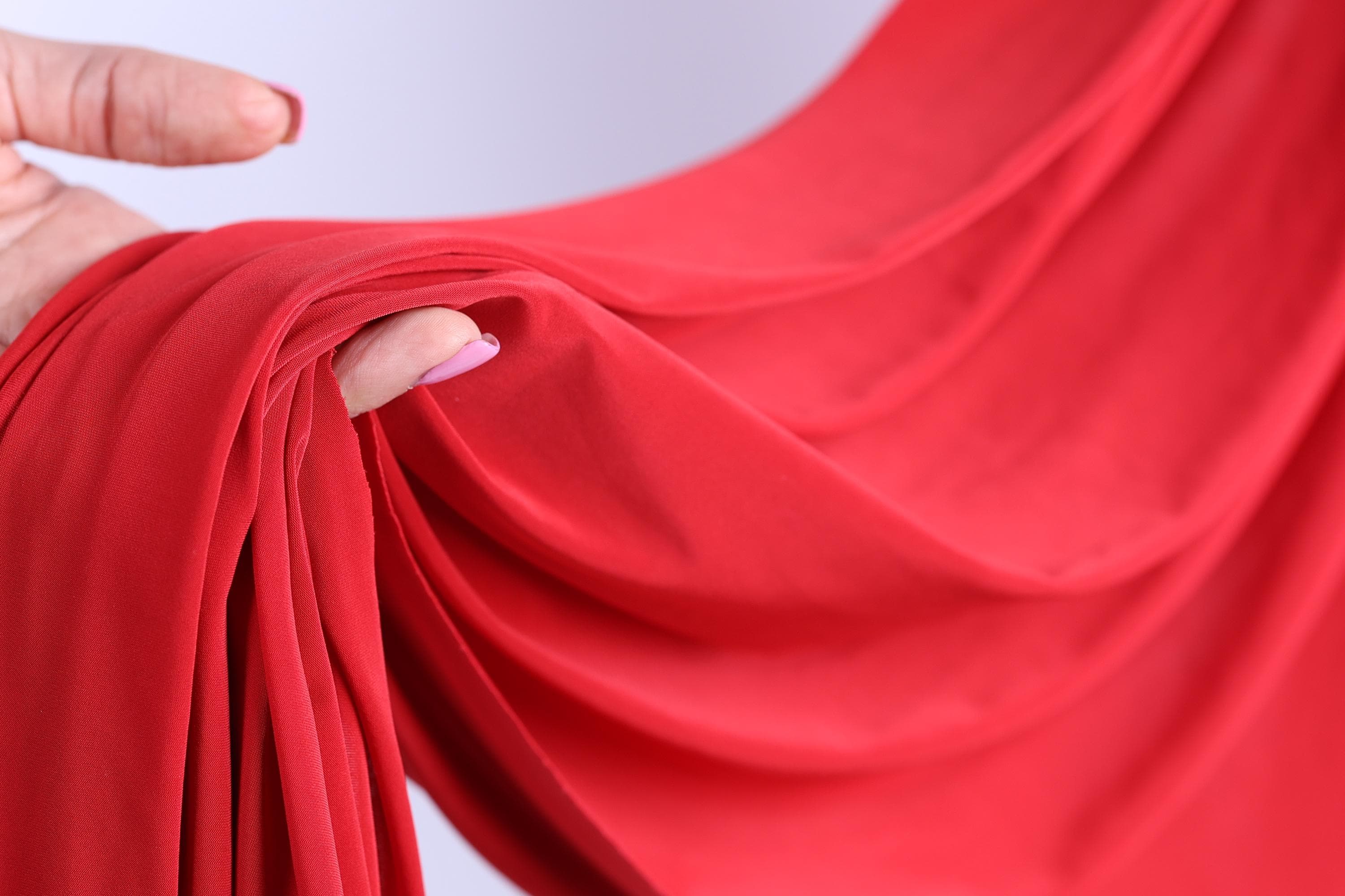 A hand is holding a red fabric, with the fingers curled around it, creating a sense of movement and texture.