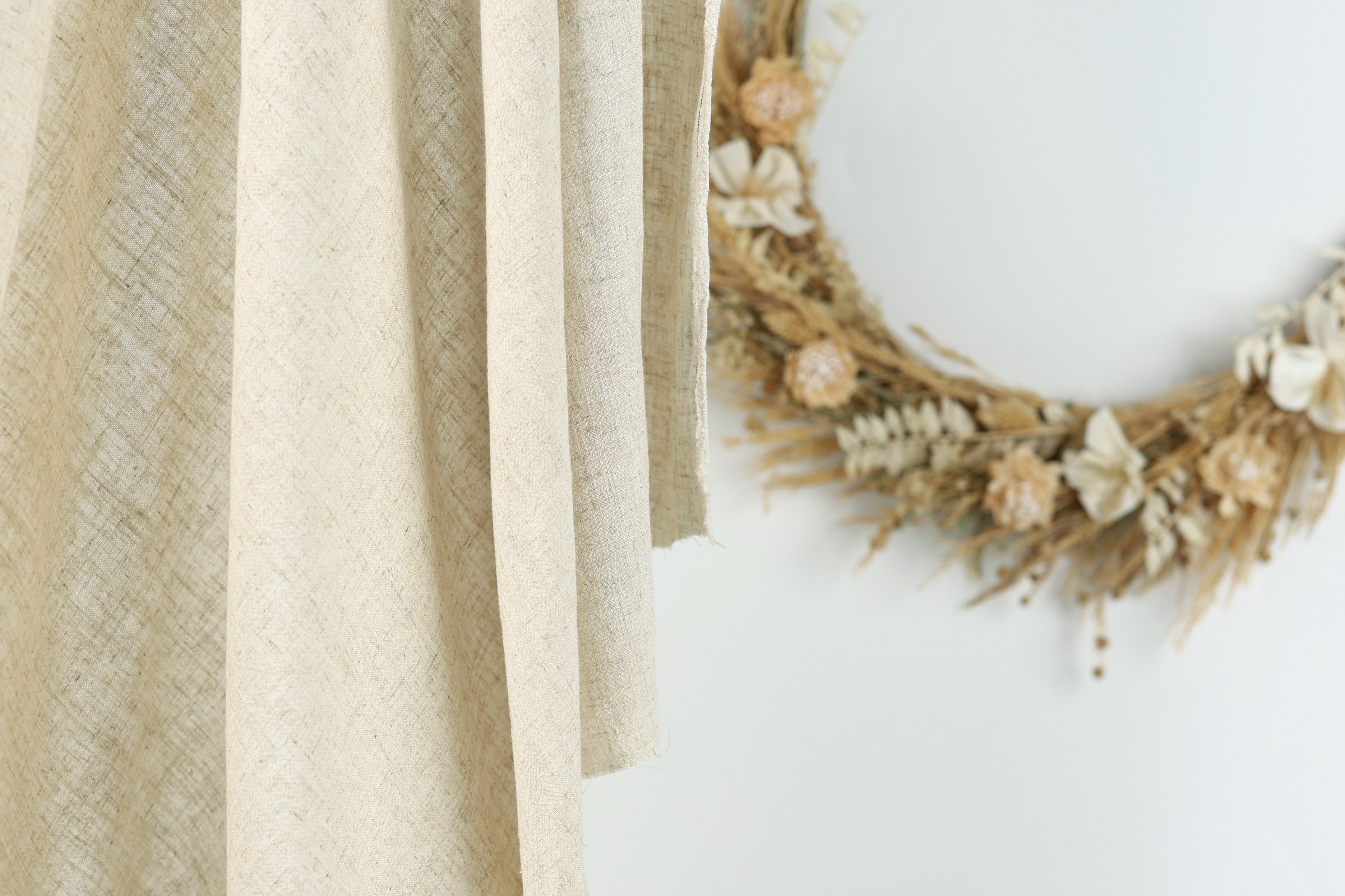 a beige fabric hanging on a wall, with a wreath made of dried flowers and branches placed next to it.