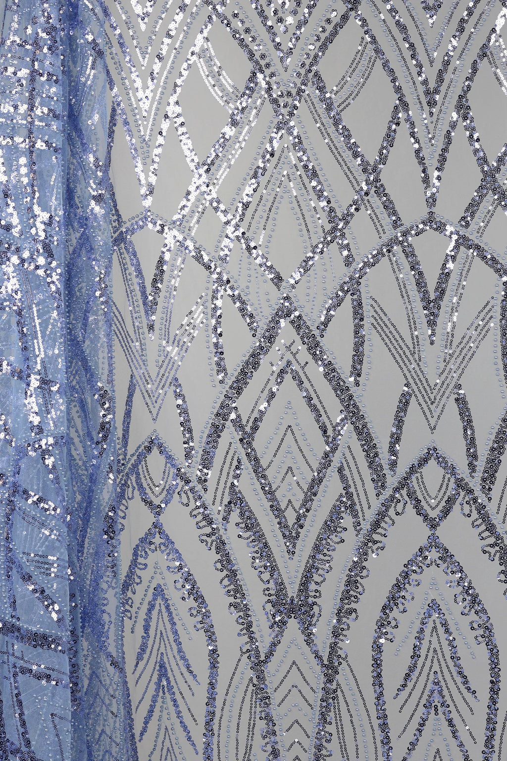 a close-up view of a fabric with a repeating pattern of silver and blue sequin designs. The pattern consists of various diamond shapes and arches, creating a visually striking and intricate design. The fabric appears to be a piece of clothing or textile, with the silver and blue sequins adding a touch of sparkle and elegance to the overall appearance.