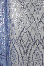 a close-up view of a fabric with a repeating pattern of silver and blue sequin designs. The pattern consists of various diamond shapes and arches, creating a visually striking and intricate design. The fabric appears to be a piece of clothing or textile, with the silver and blue sequins adding a touch of sparkle and elegance to the overall appearance.