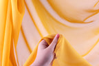 A hand holding a yellow fabric against a blurred background of yellow fabric.