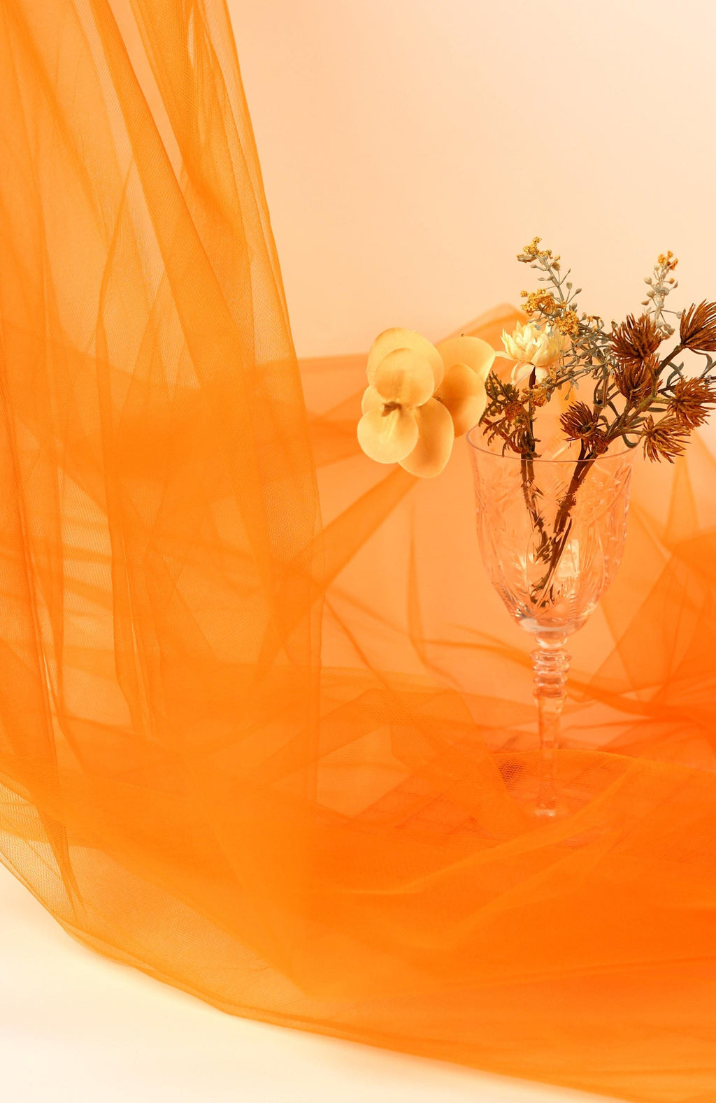 a glass vase with flowers and a tulip, set against an orange background.