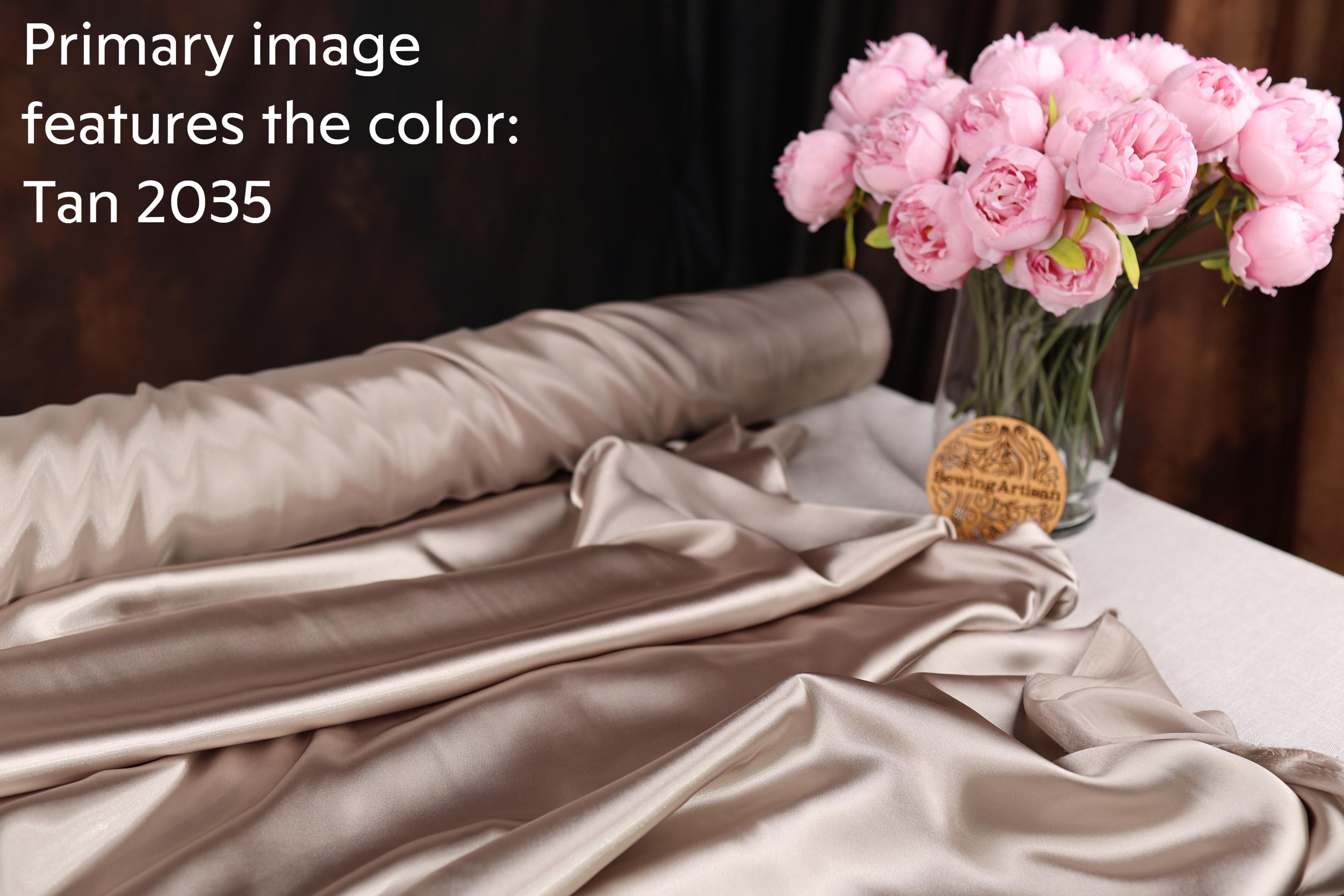 a bouquet of pink flowers in a glass vase, placed on a table with a roll of fabric and a wooden plaque.