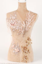 A mannequin with a beige body and a white head, adorned with intricate floral and leaf embroidery in shades of pink and gold.