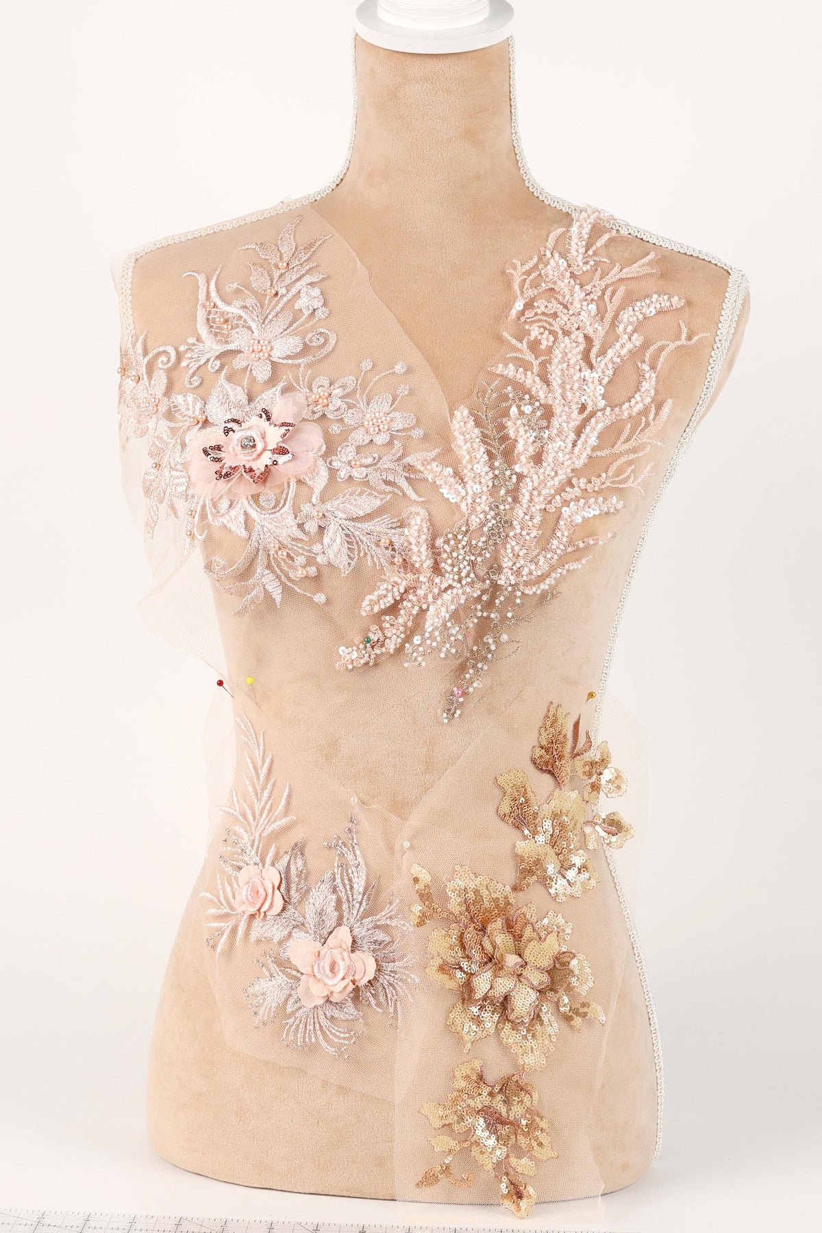 A mannequin with a beige body and a white head, adorned with intricate floral and leaf embroidery in shades of pink and gold.