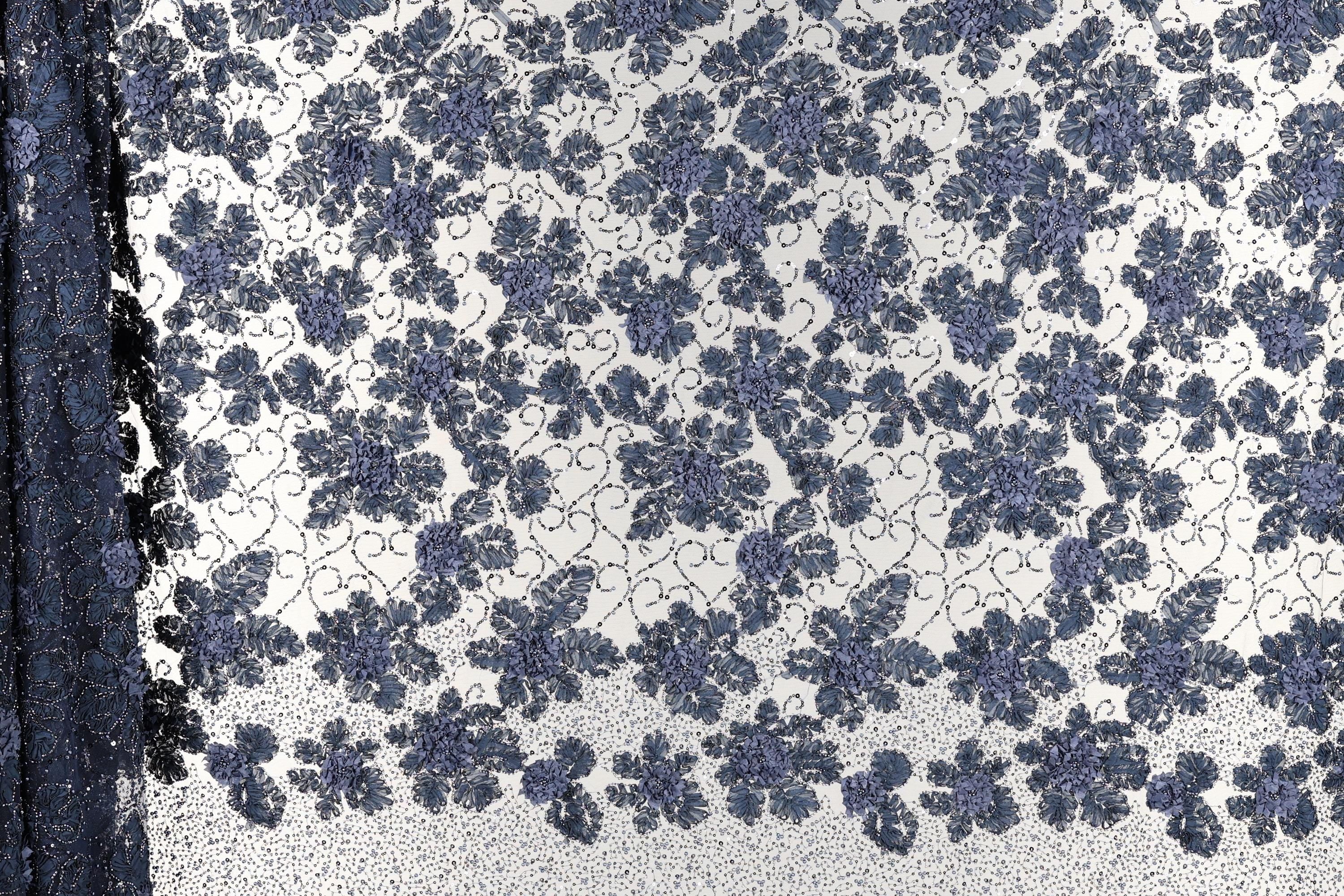 a close-up view of a fabric with a floral pattern. The fabric appears to be a blend of blue and white colors, with a repeating floral design that creates a visually appealing and intricate pattern.