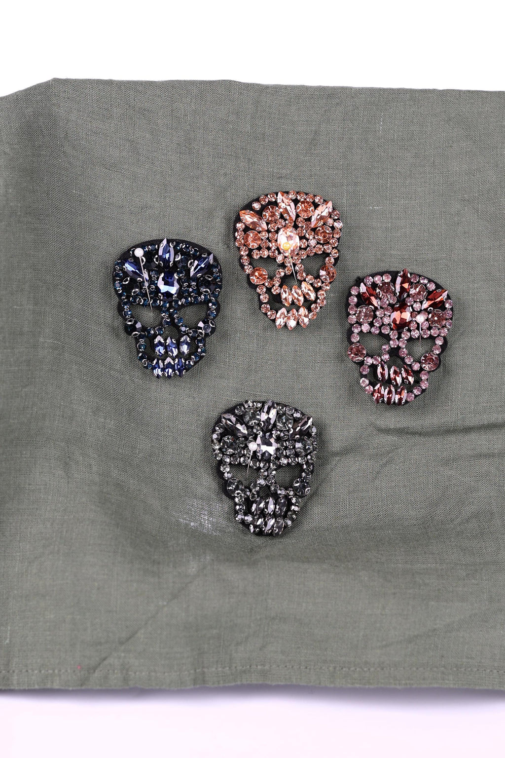 four ornate skull-shaped brooches, each adorned with a variety of colorful gemstones.