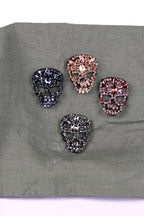 four ornate skull-shaped brooches, each adorned with a variety of colorful gemstones.