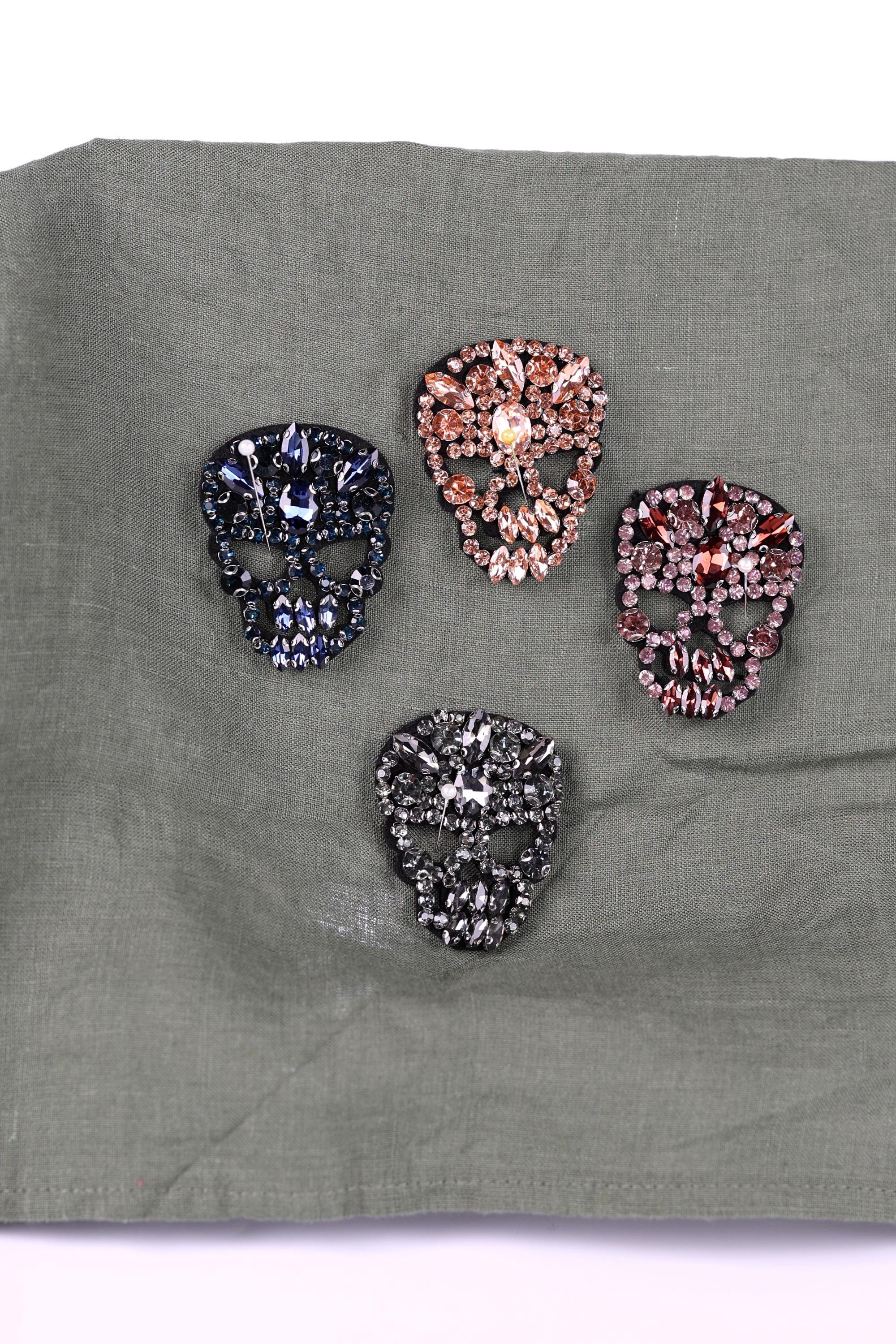 four ornate skull-shaped brooches, each adorned with a variety of colorful gemstones.