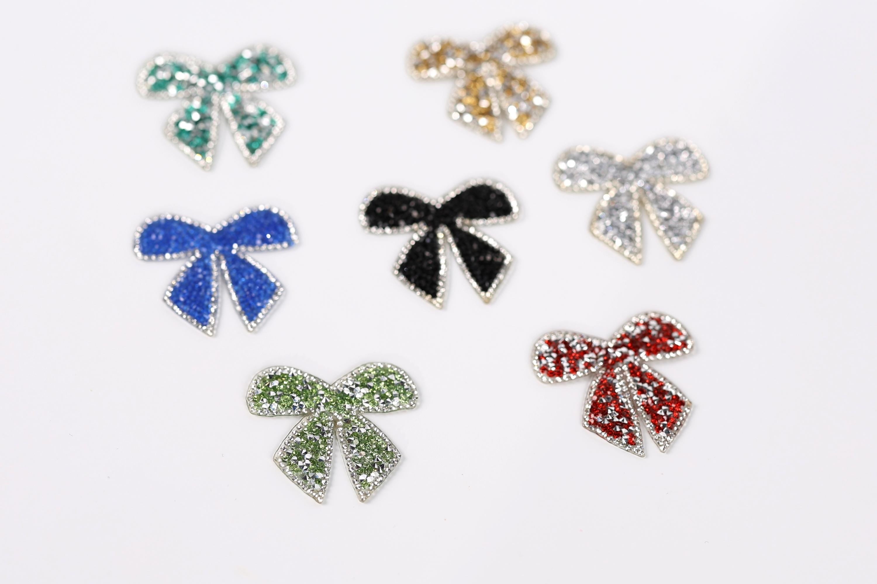 six small, colorful, and sparkling bow-shaped objects arranged on a white background.
