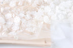 The image is a close-up of a delicate, white lace fabric with intricate floral embroidery. The fabric appears to be a light pink color, and the flowers are arranged in a way that creates a sense of depth and texture. The image does not contain any discernible objects or actions, and the focus is solely on the lace fabric and its floral design.