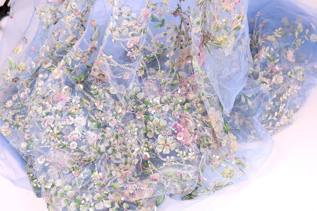 The image is a close-up of a delicate, intricately embroidered fabric with a floral pattern. The fabric appears to be made of a sheer, light-colored material, giving it a soft and delicate appearance. The embroidery features a variety of flowers and leaves in different colors, creating a visually appealing and detailed design.