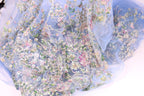 The image is a close-up of a delicate, intricately embroidered fabric with a floral pattern. The fabric appears to be made of a sheer, light-colored material, giving it a soft and delicate appearance. The embroidery features a variety of flowers and leaves in different colors, creating a visually appealing and detailed design.