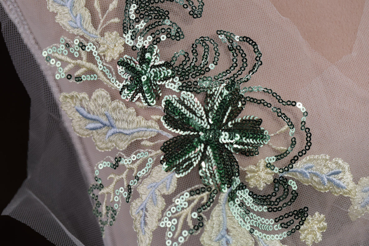a close-up view of a delicate, intricate embroidered design on a fabric. The design features a floral pattern with green and white sequins, creating a visually appealing and detailed piece of textile art.