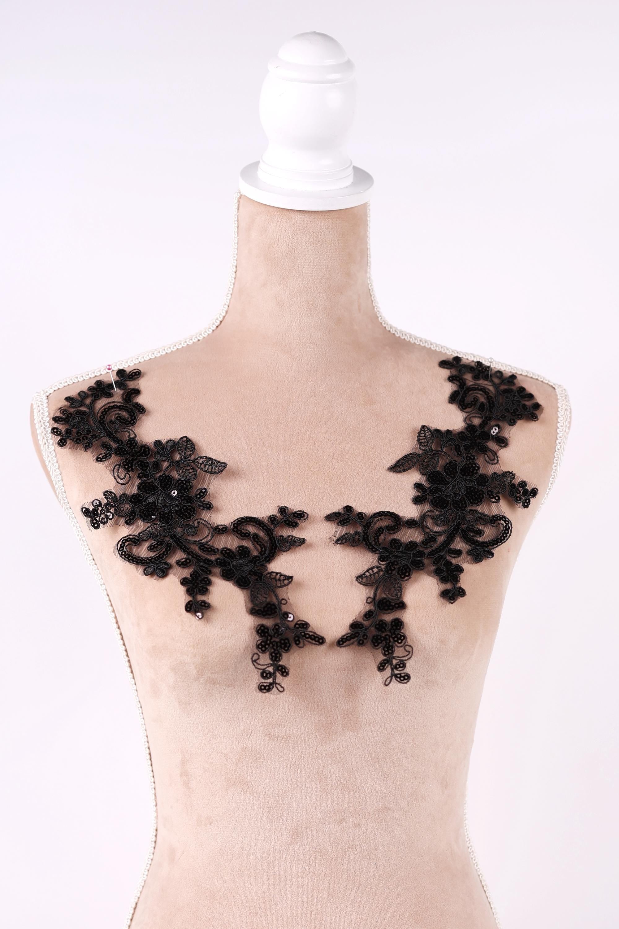 A mannequin wearing a beige dress with black lace appliques on the shoulders.
