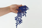 A hand holding a piece of blue lace against a white background.
