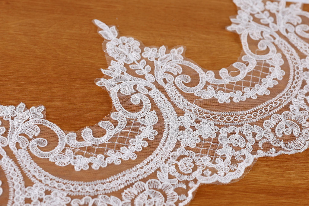 A close-up view of a delicate, intricately designed white lace fabric with floral patterns.