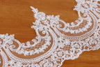 A close-up view of a delicate, intricately designed white lace fabric with floral patterns.