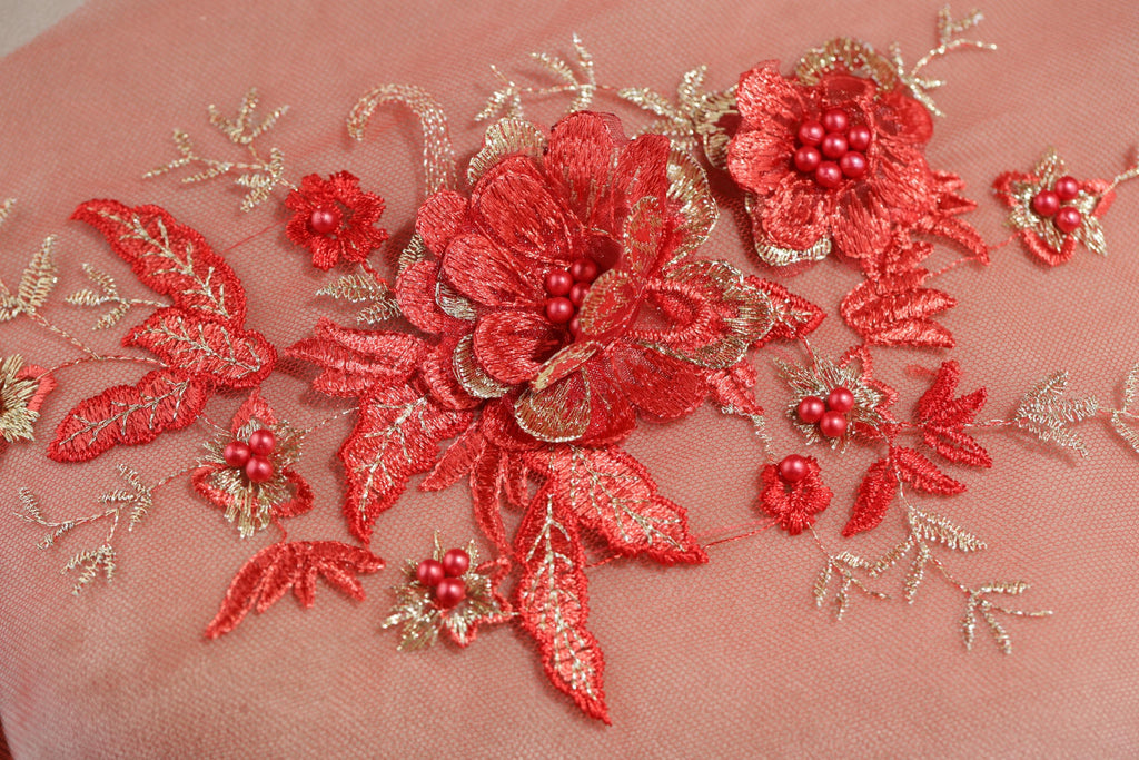 a close-up view of a delicate, intricately embroidered floral design on a pink fabric. The design is composed of various red flowers and leaves, with some adorned with small red berries. The embroidery is detailed and appears to be handcrafted, showcasing the skill and artistry involved in creating this beautiful textile art piece.