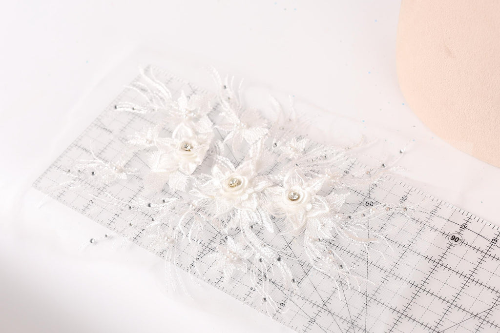 a close-up view of a delicate white lace flower with a small crystal center, placed on a transparent ruler.